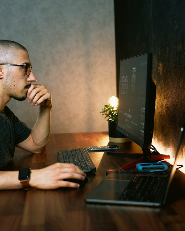 Male Sitting in front of a Desktop and Laptop Computer
